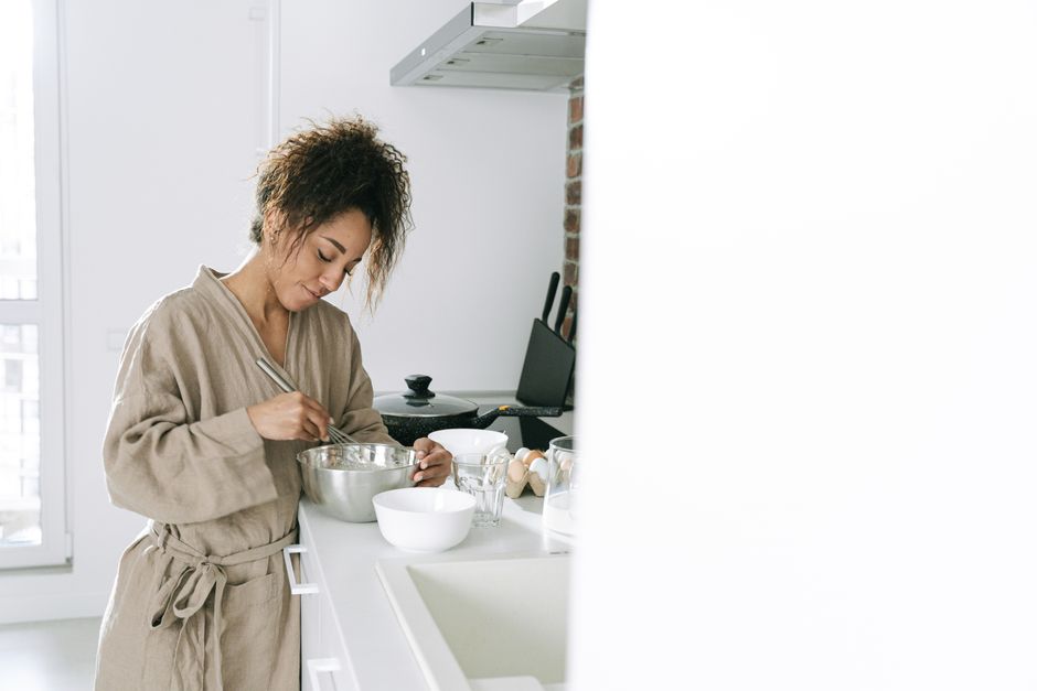 A young woman prepares food in a stylish white kitchen, mixing ingredients in a bowl.