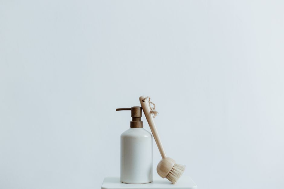 A minimalist soap dispenser and wooden brush set against a plain white background.